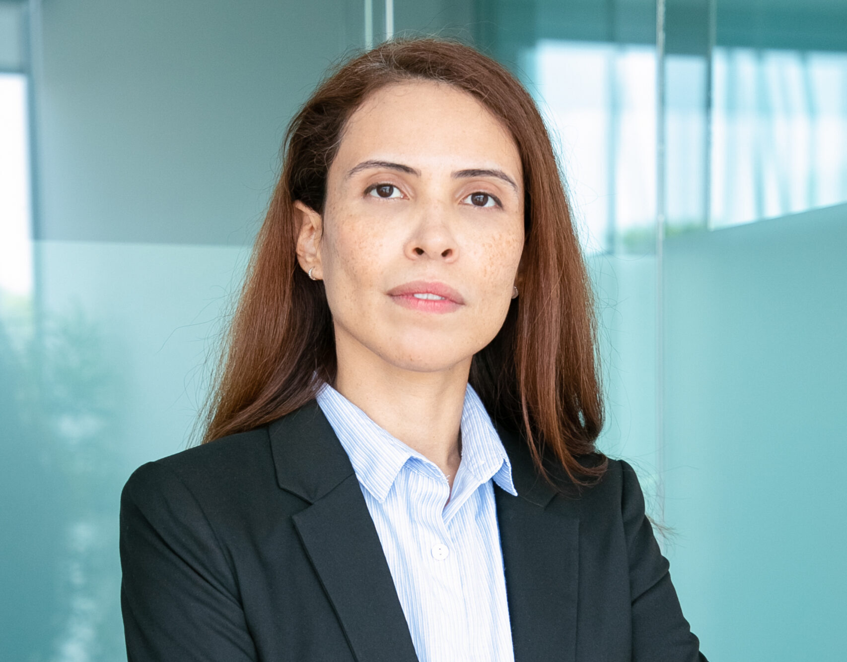 Serious confident red haired business lady wearing jacket, standing with arms folded and looking at camera. Medium shot, vertical. Business portrait concept